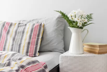 a bed and nightstand with a vase of flowers