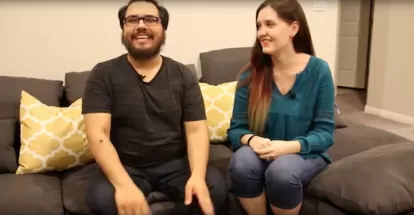 a young couple sits on a couch in their home